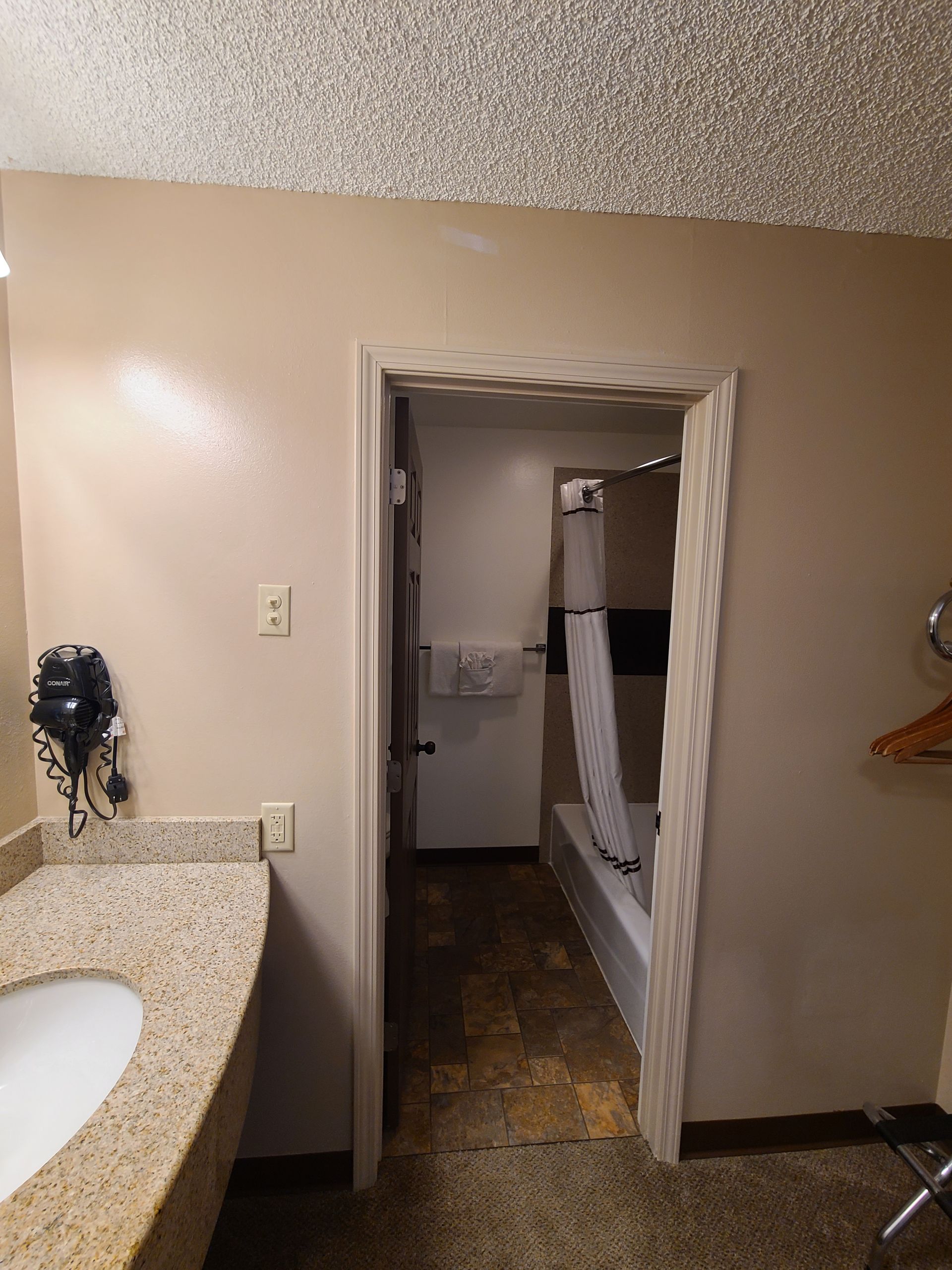 Bathroom with doorway to tub/shower area, beige walls, granite countertop, and floor.