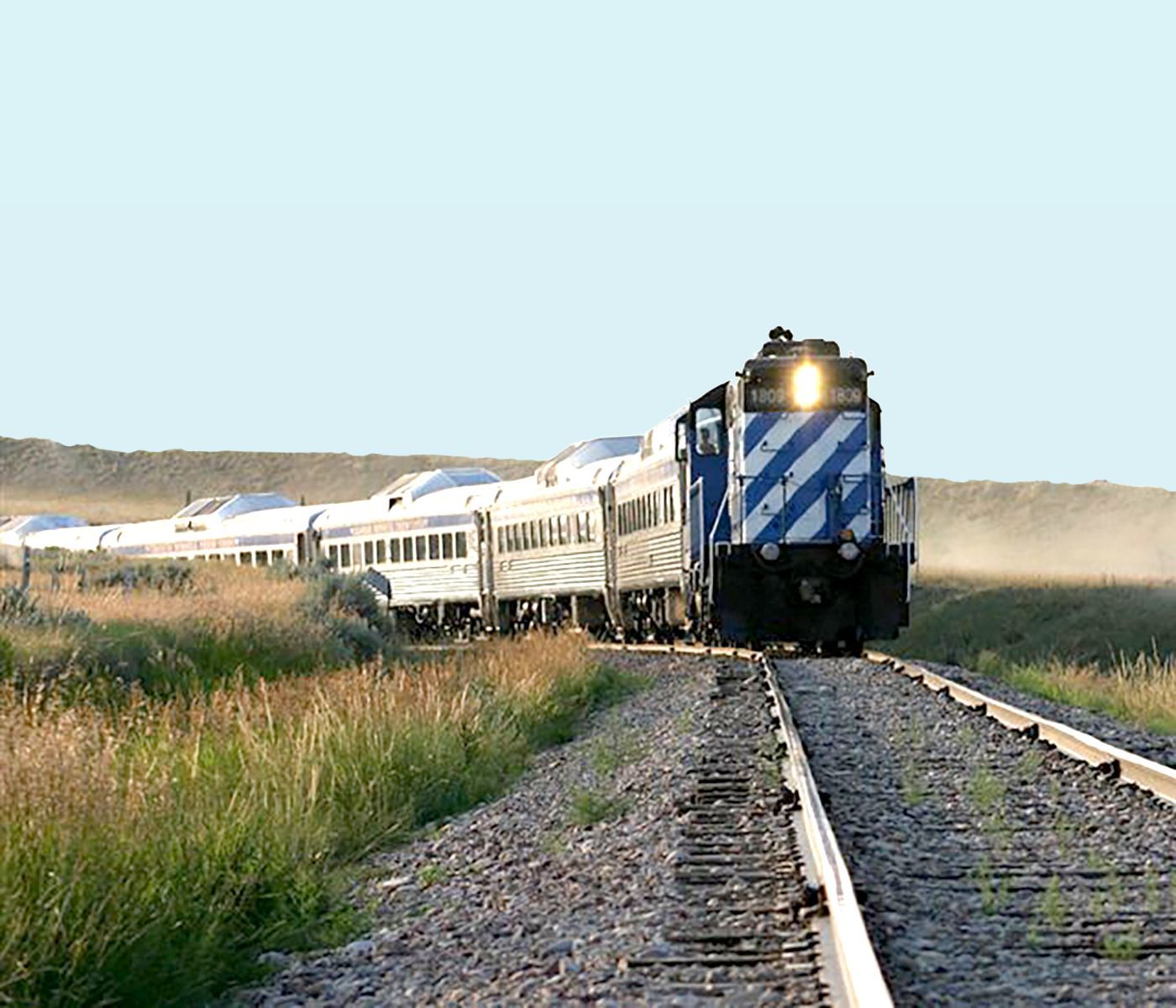 Train traveling on tracks through grassy landscape, blue and white engine, clear sky.