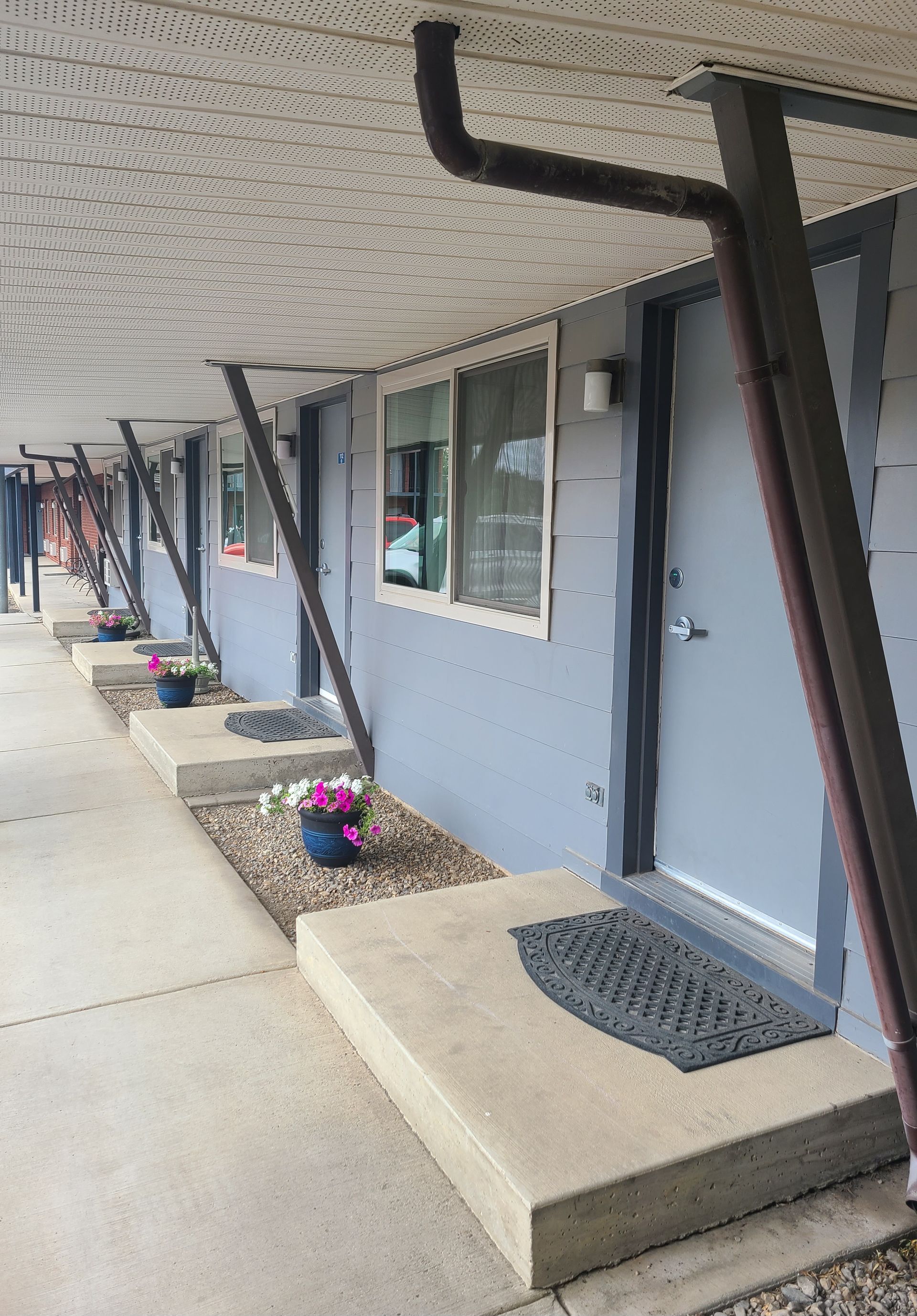 Exterior view of an apartment complex with gray doors, concrete steps, and a covered walkway.