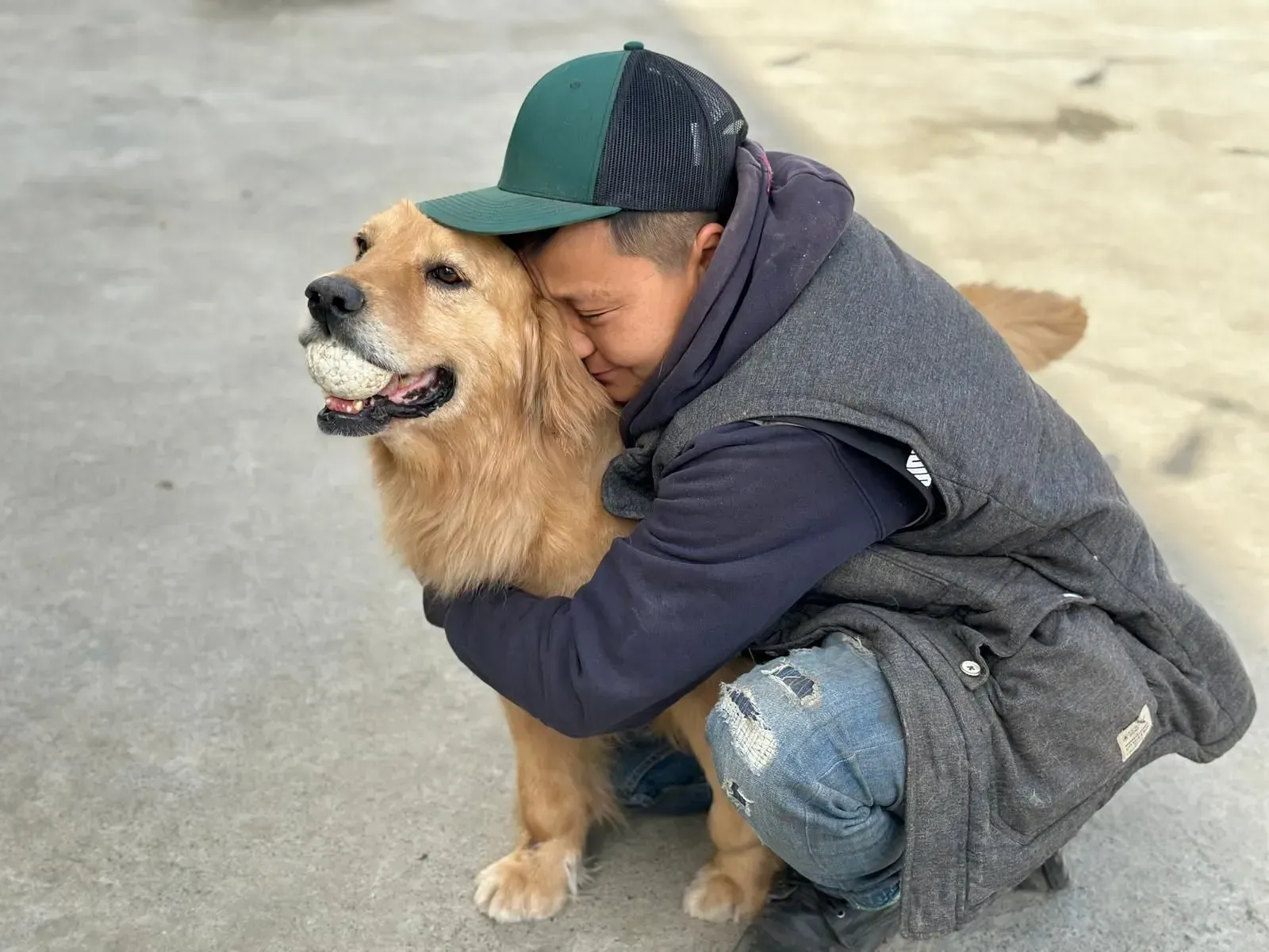 Child hugging a golden dog outdoors on pavement, both sitting close together