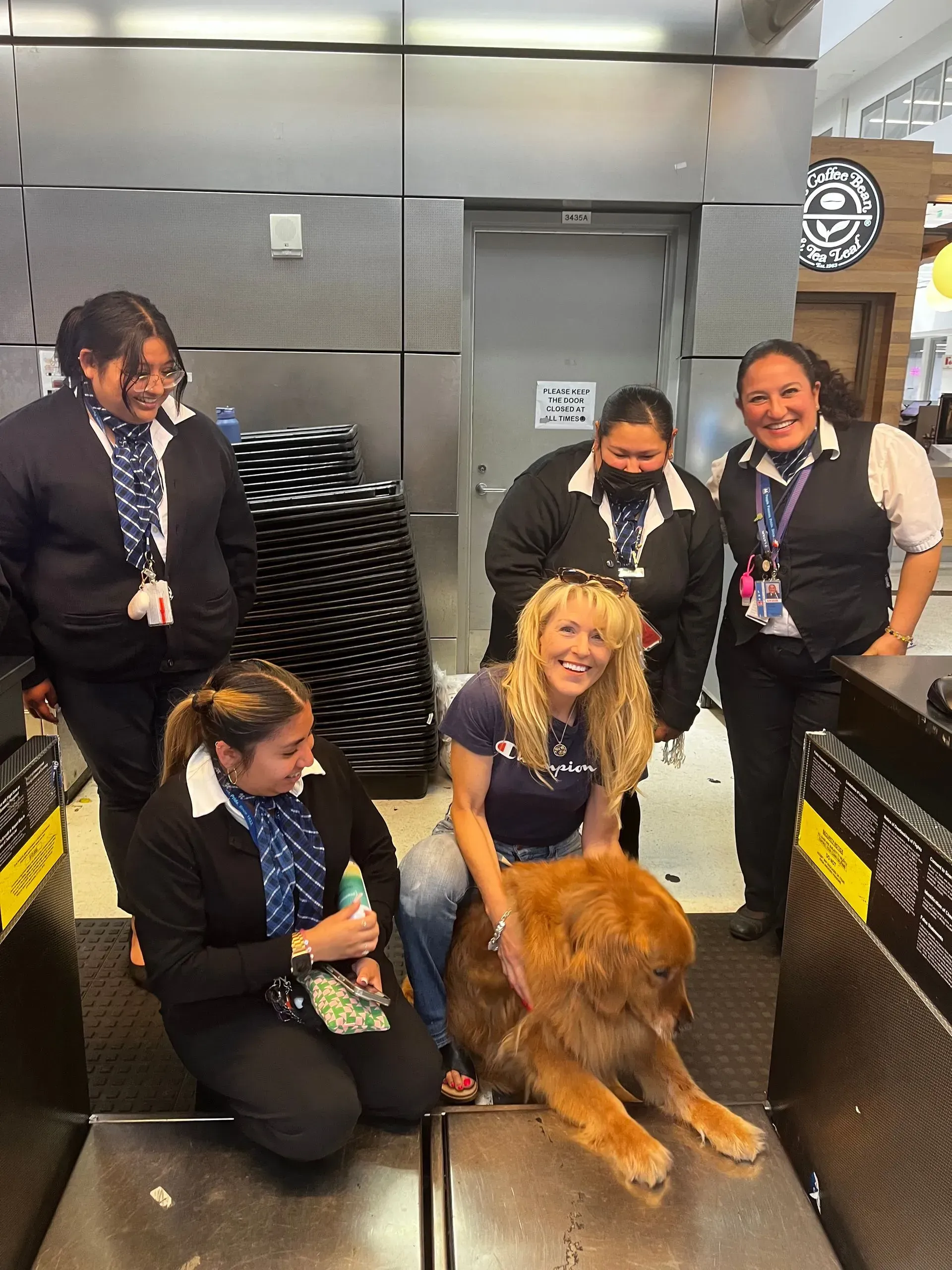 Five people in uniforms kneel and stand with a golden retriever in a metal-walled room