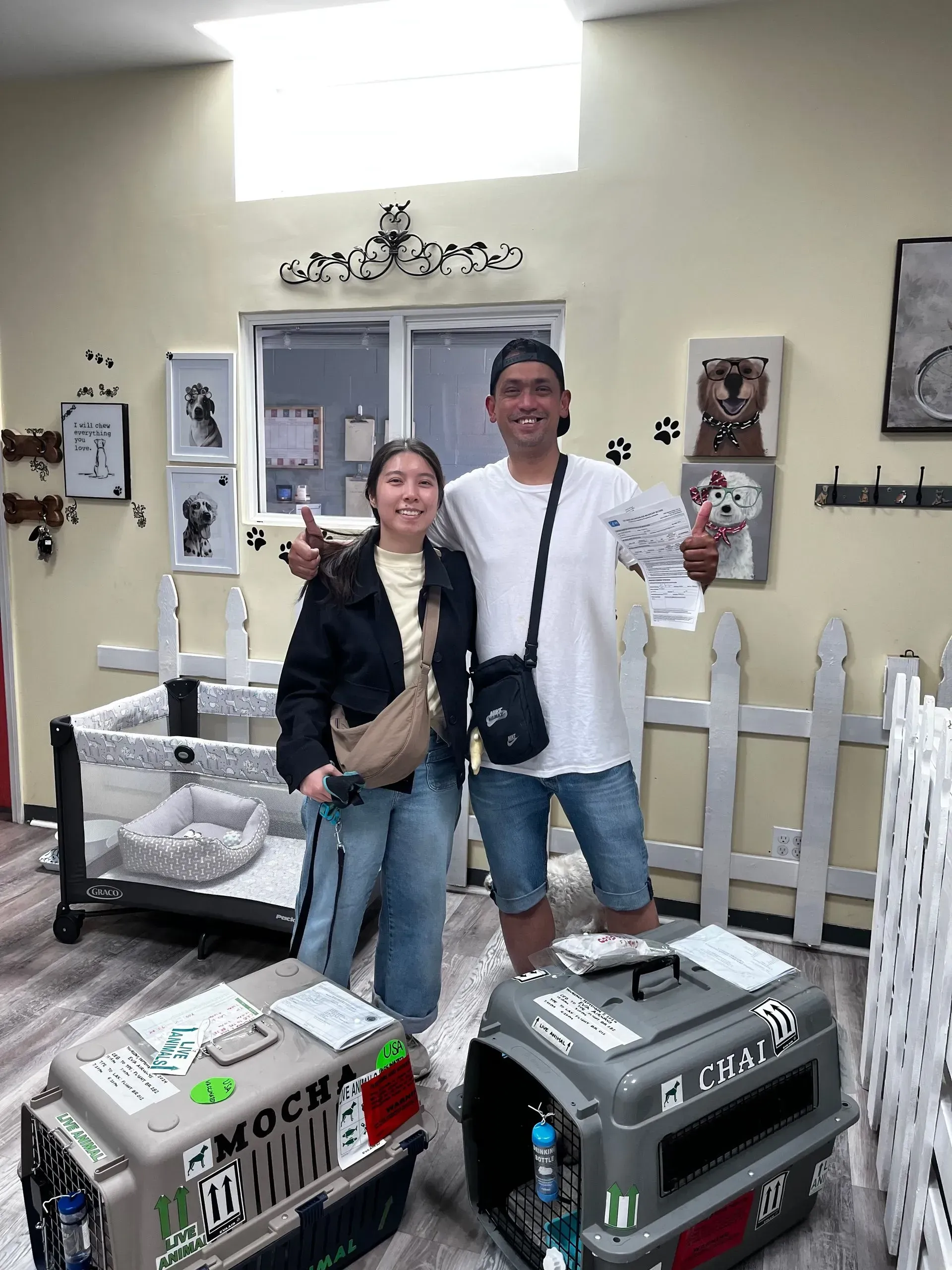 Two people standing in a pet-store aisle beside large animal carriers and small animals in cages.