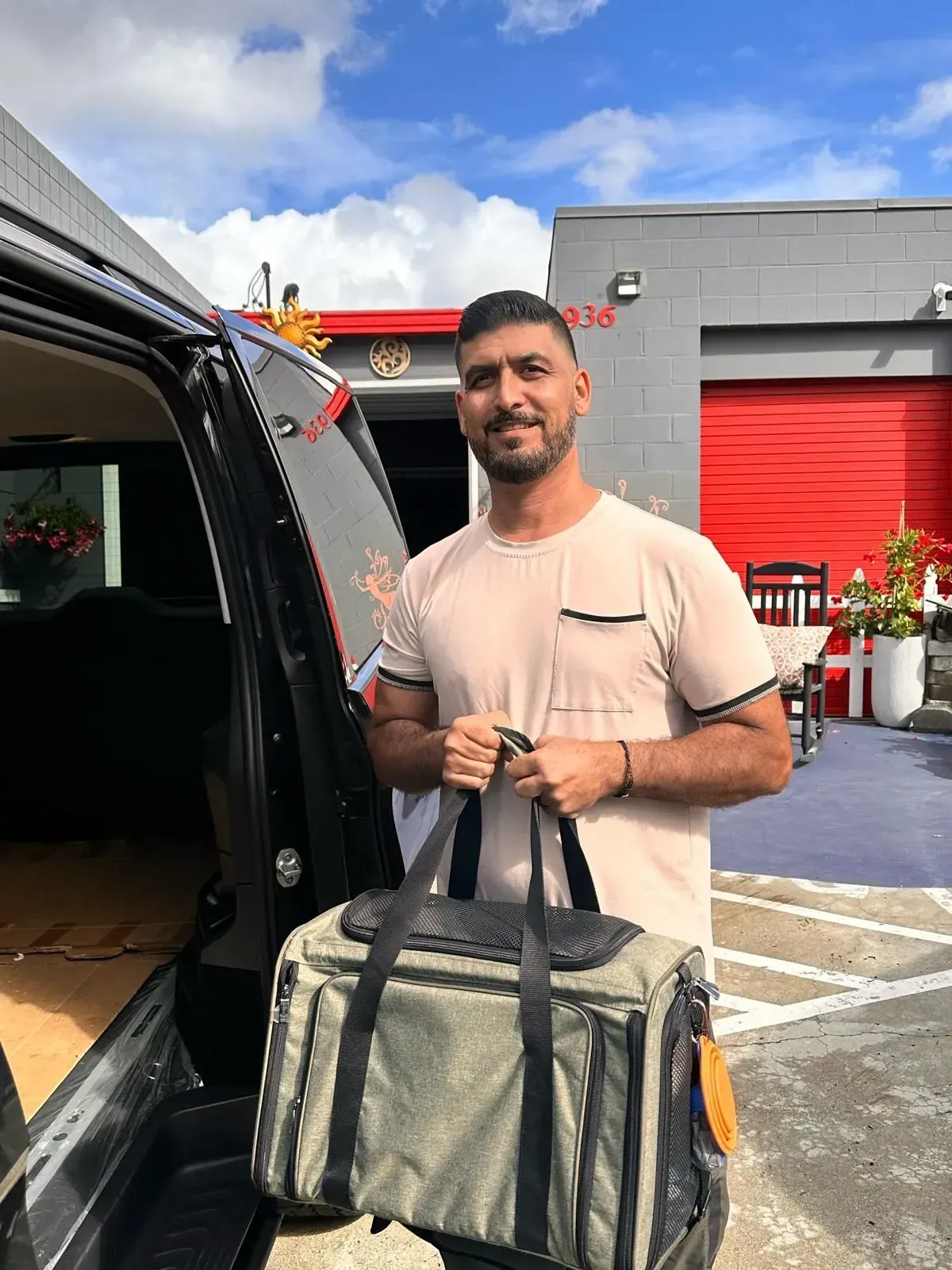 Man loading a gray duffel bag into the back of a black van outside a building