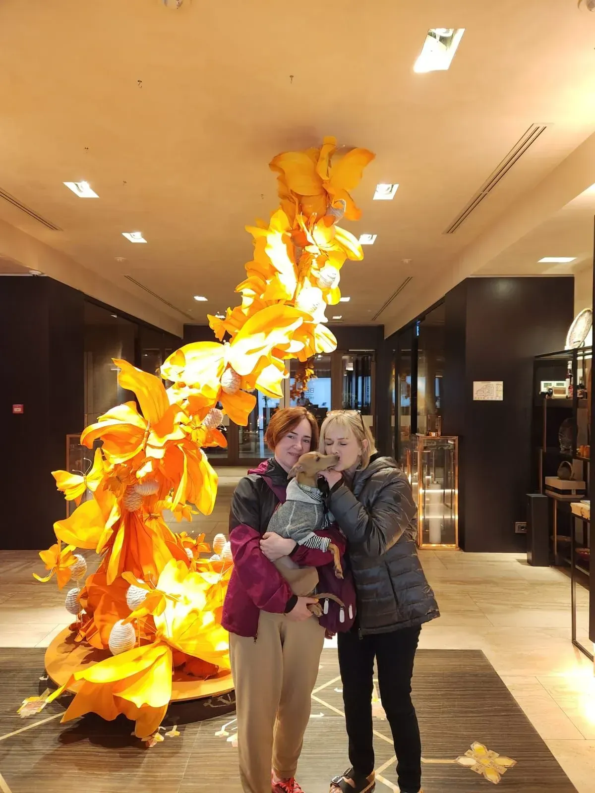 Two people posing indoors beside a tall orange hanging sculpture in a modern lobby