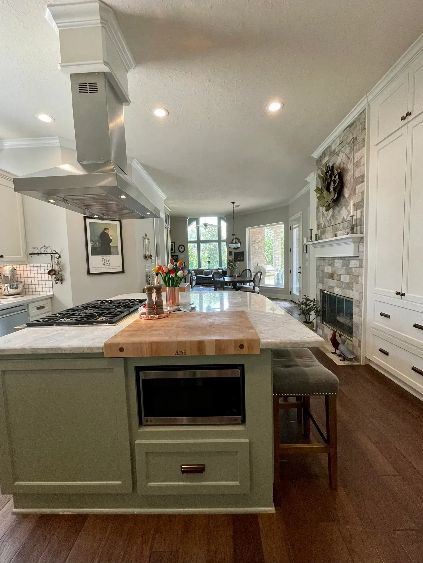 Bright modern kitchen with a large island, white cabinetry, wood floors, and stainless-steel range hood.
