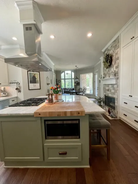 Bright modern kitchen with a large island, white cabinetry, wood floors, and stainless-steel range hood.