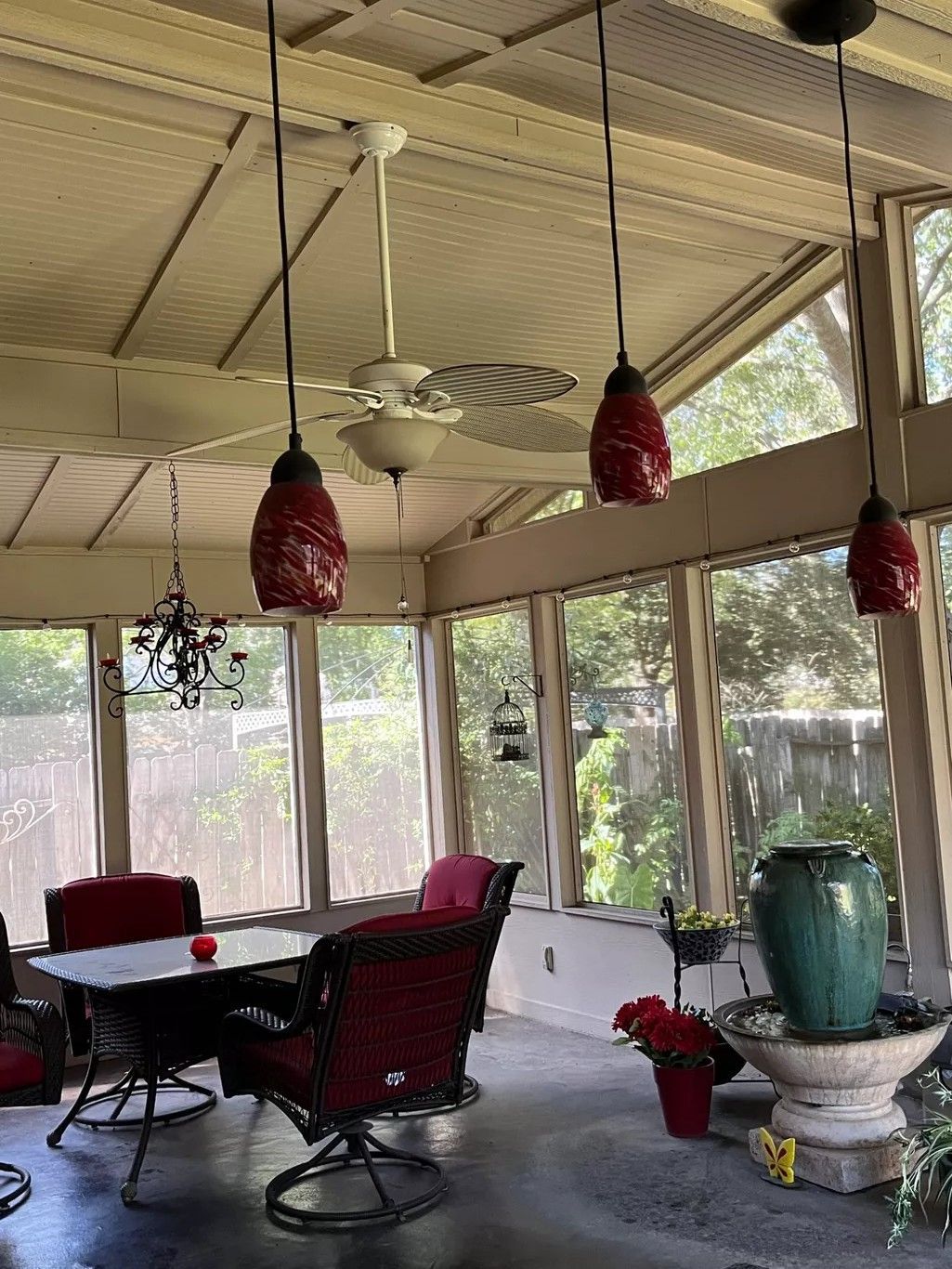 Screened porch with red chairs, round table, hanging lanterns, and a fountain beside large windows.