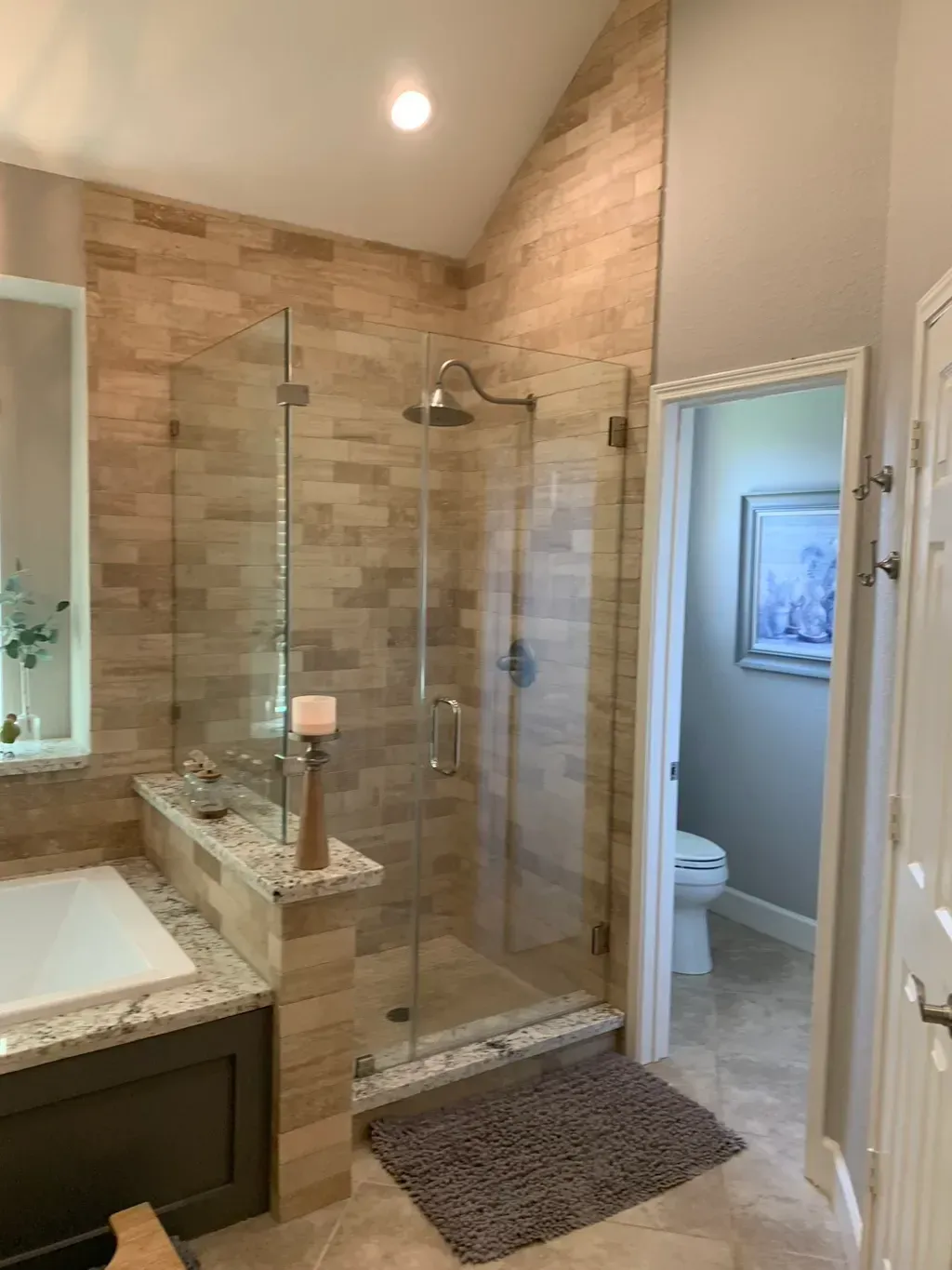 Tiled walk-in shower with glass door beside a vanity and open bathroom doorway.
