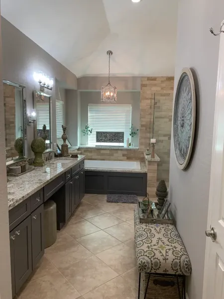 Elegant bathroom with double vanity, tiled floor, bathtub under window, and bench with patterned cushion.