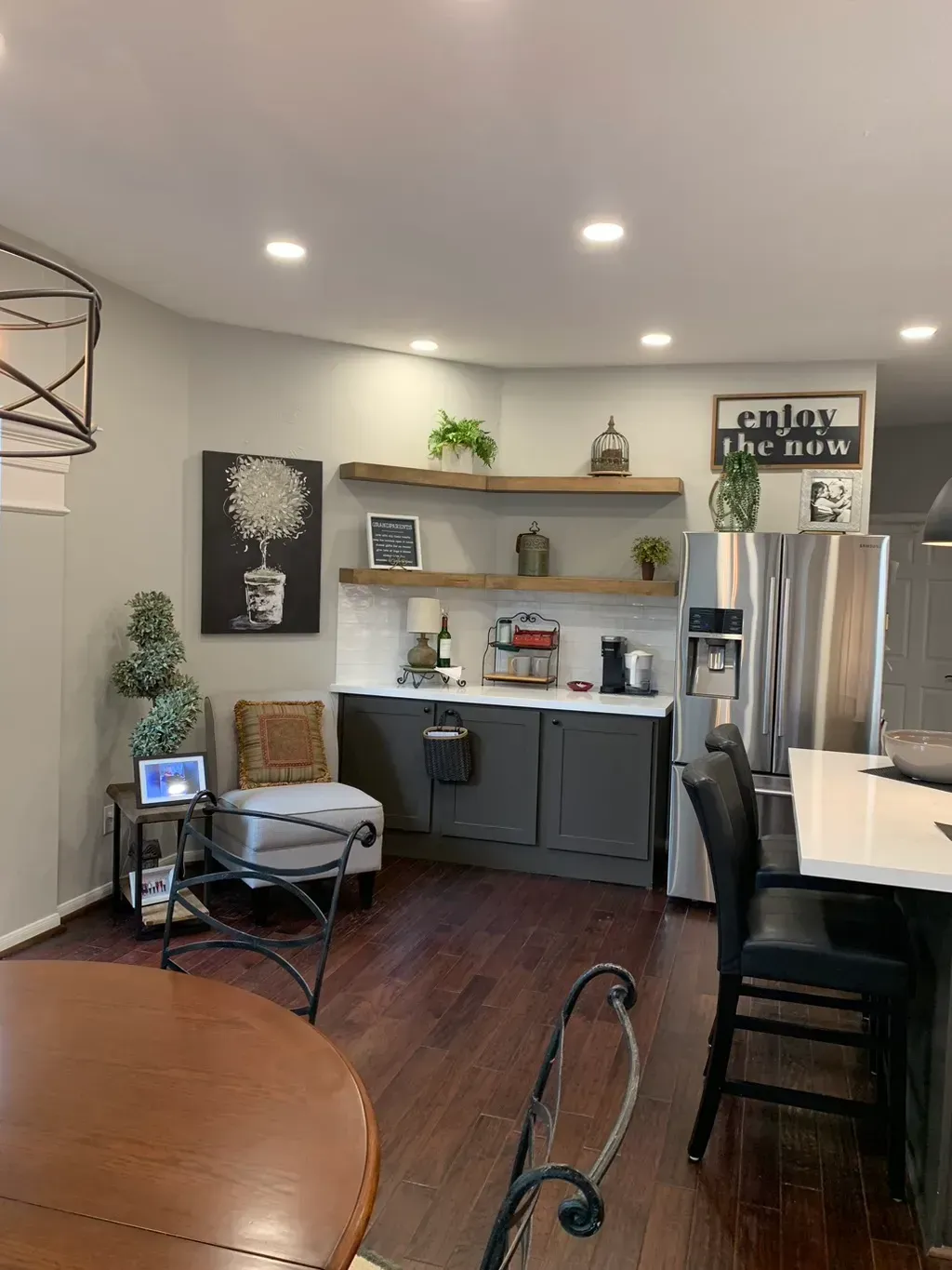 Modern kitchen and dining area with stainless fridge, gray cabinets, shelves, and wooden table under recessed lights