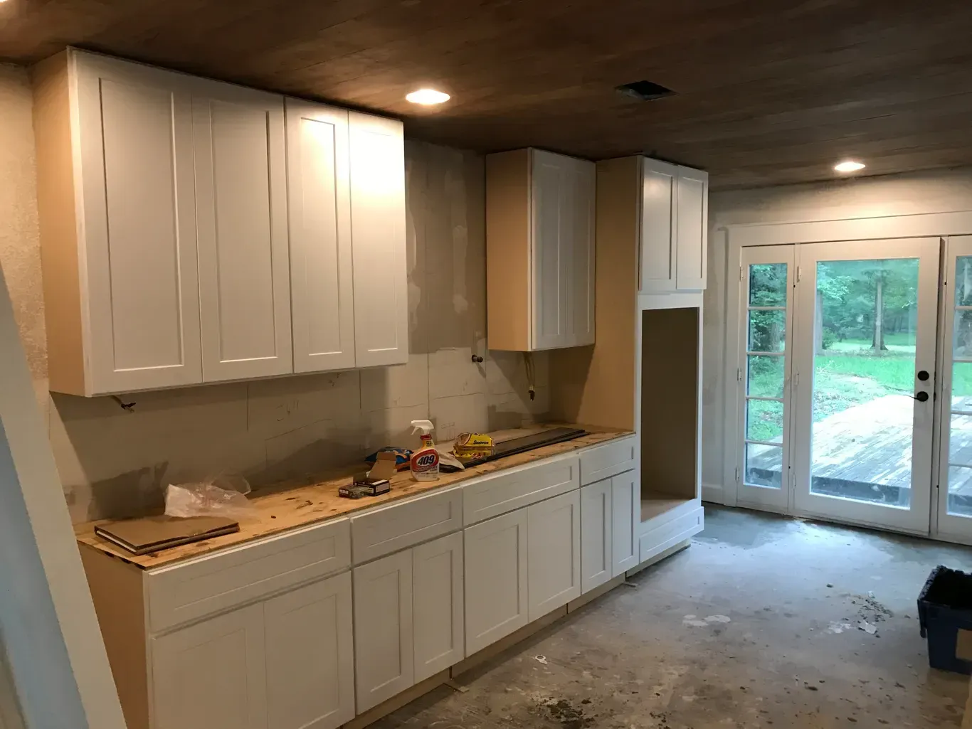 Bright kitchen with white cabinets, wood ceiling, and glass doors opening to a backyard.