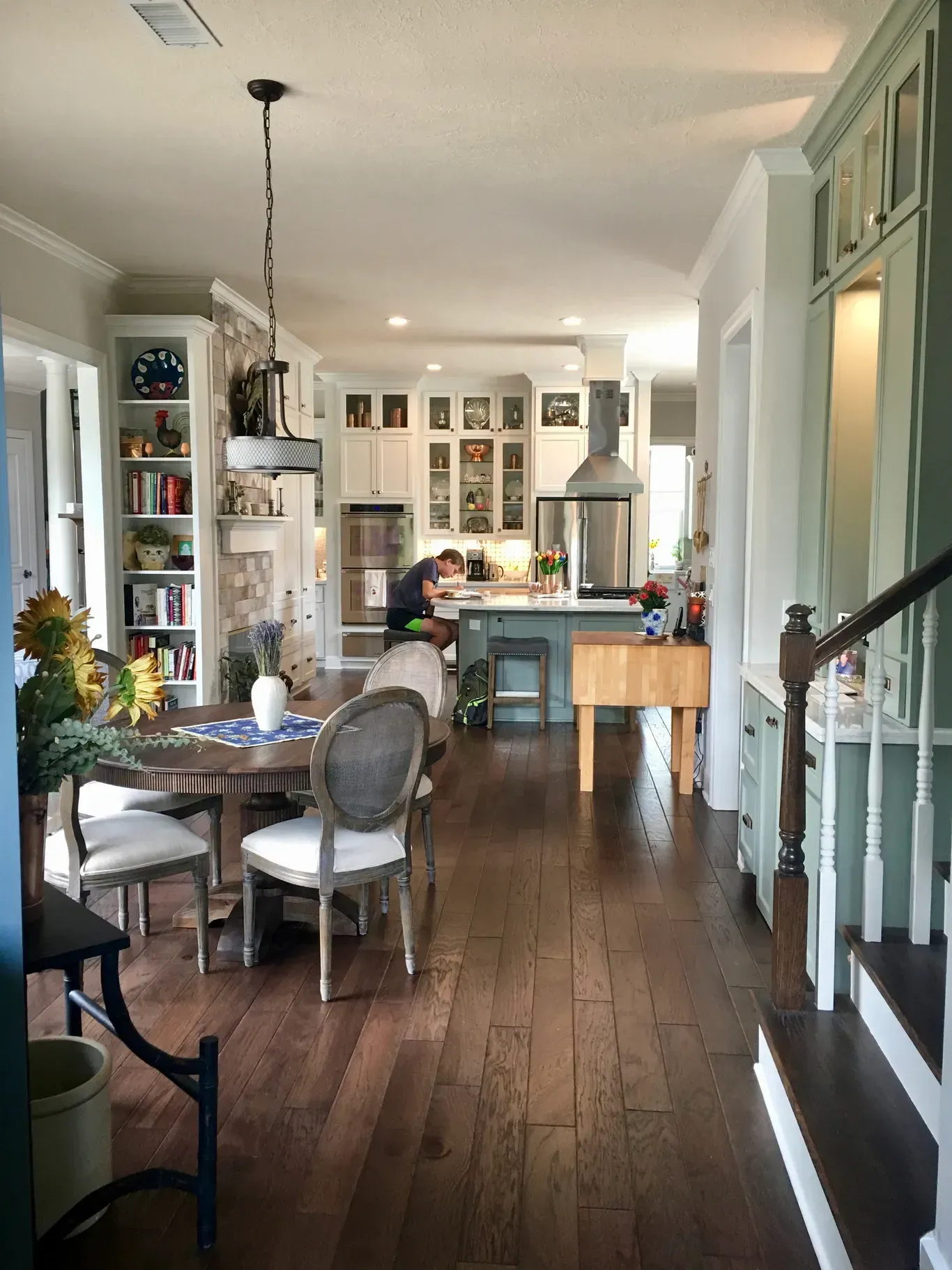 Bright open kitchen and dining area with hardwood floors, white cabinets, and a person seated at the table.