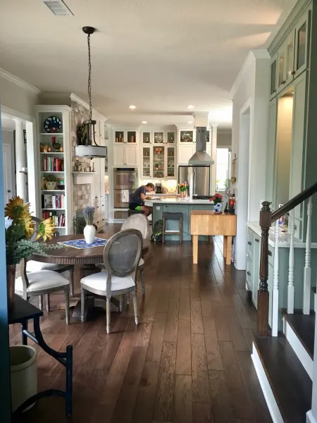 Bright kitchen and dining area with dark wood floors, white cabinets, and a table set near a staircase.