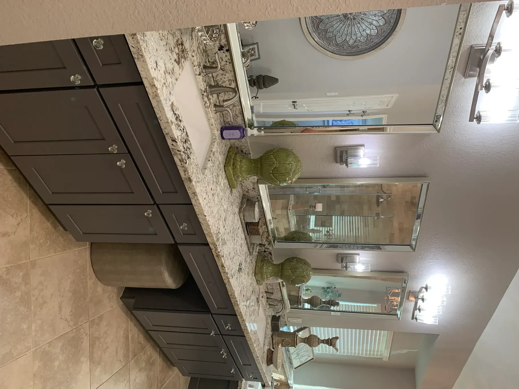 Bathroom vanity with double sinks, large mirrors, and dark cabinets under bright lights