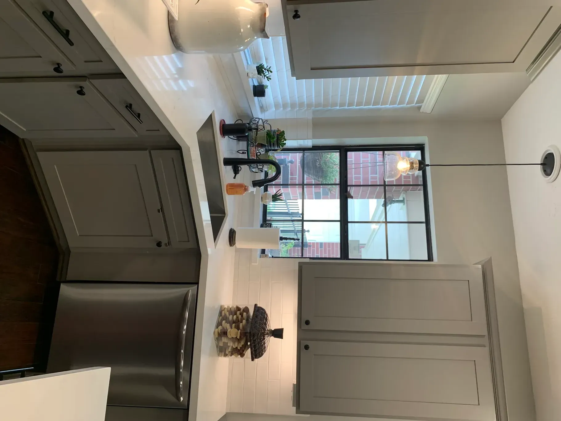 Modern kitchen with gray cabinets, white island, stainless fridge, and large window by a dining area