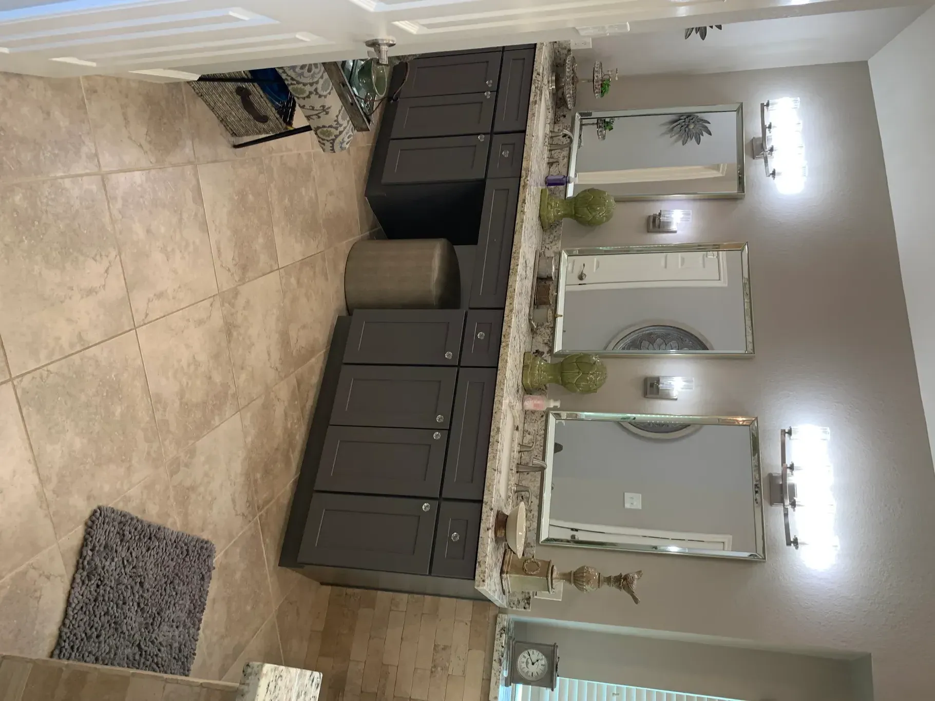 Modern bathroom vanity with double sinks, beige tile floor, mirrors, and wall sconces