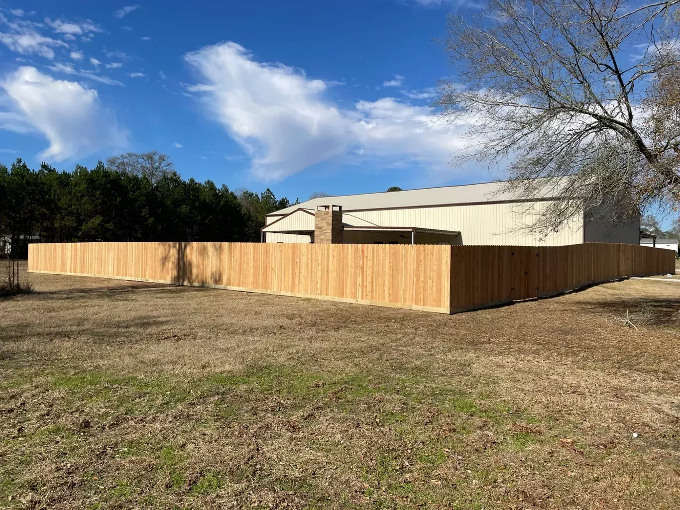 Wooden privacy fence around a beige house in a grassy yard under a blue sky