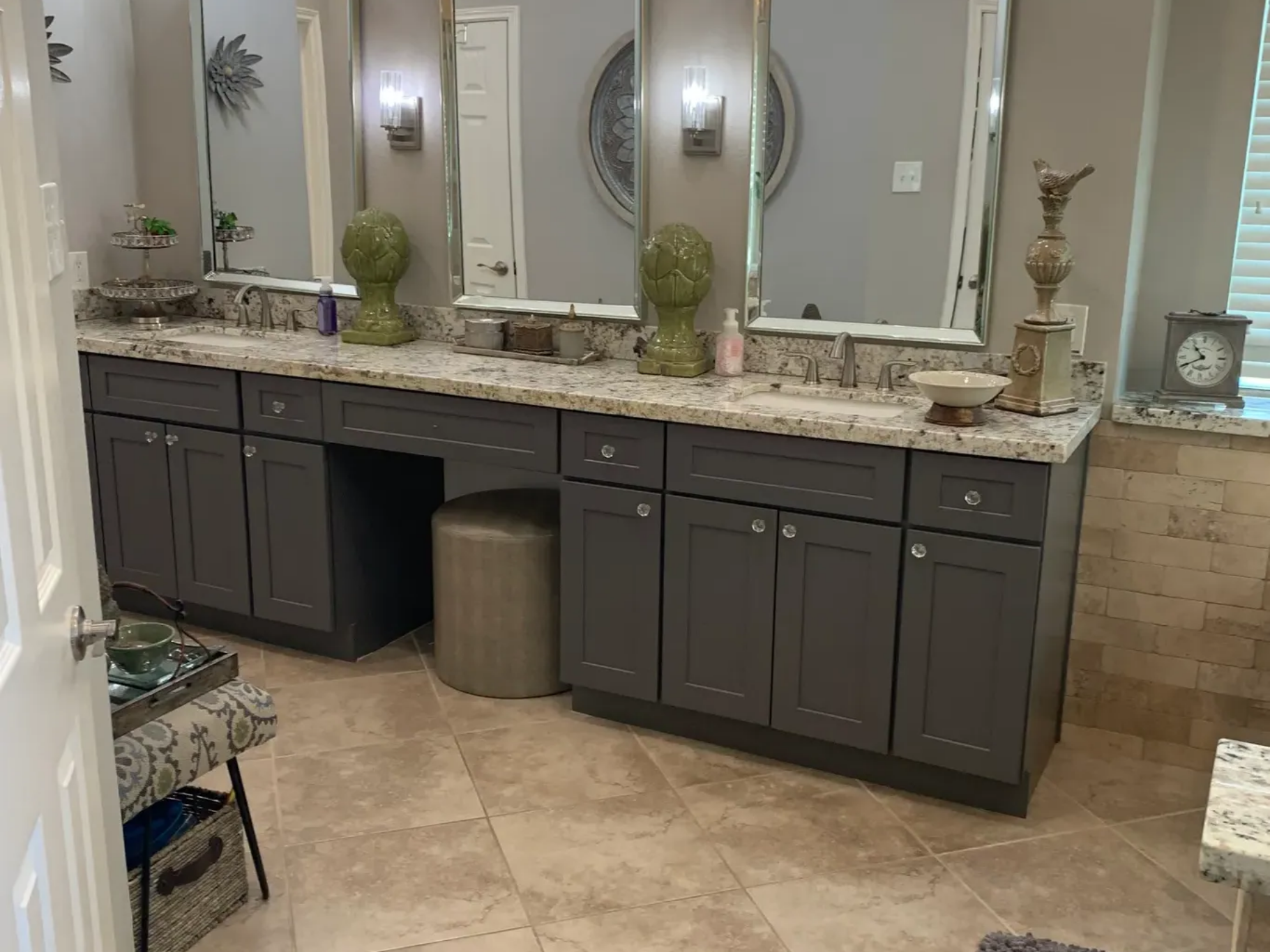 Bathroom vanity with dark cabinets, granite countertop, mirrors, and decorative accents