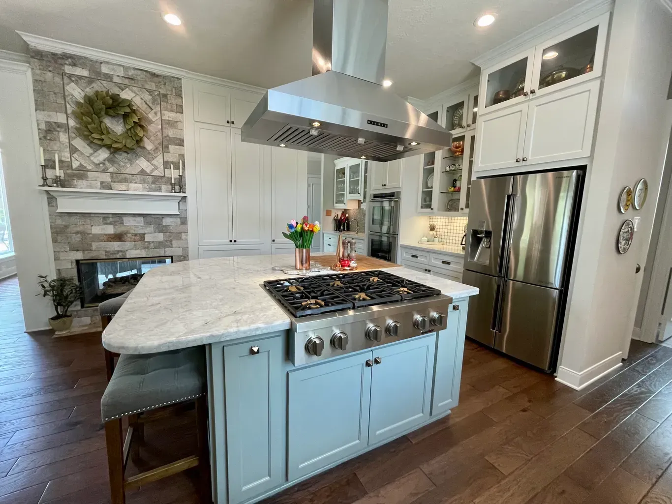 Bright modern kitchen with marble island, blue cabinets, stainless steel appliances, and hardwood floors