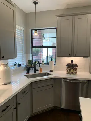 Bright white kitchen corner with gray cabinets, window over sink, and stainless dishwasher