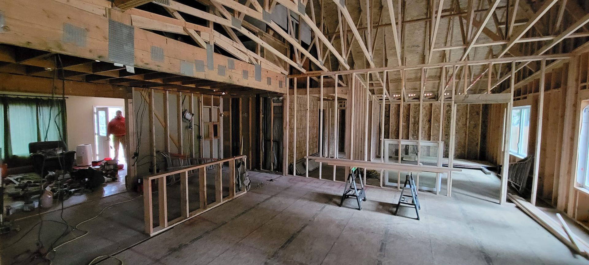 Interior view of a residential construction site featuring wood framing, exposed wall studs, and rafters under renovation.