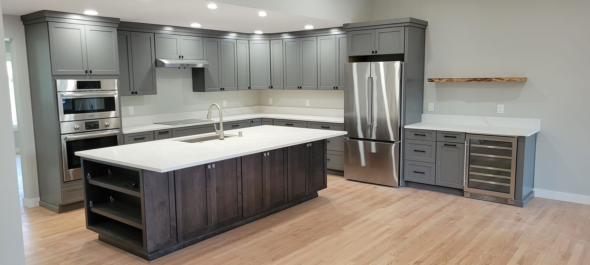 A modern kitchen featuring gray cabinets, white countertops, a large island, and stainless steel appliances.
