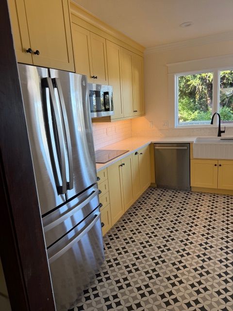A bright yellow kitchen with stainless steel appliances, a farmhouse sink, and a geometric-patterned tile floor.