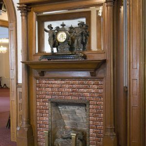 Brick fireplace with carved wooden mantel and a decorative clock in a paneled room