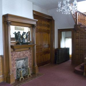 Interior hallway with wood paneling, fireplace, staircase, and chandelier in a historic home