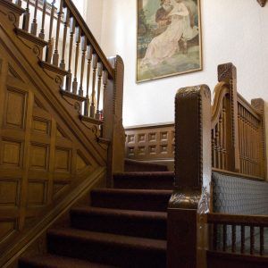 Wood-paneled staircase with carved banisters and a framed painting on the landing.