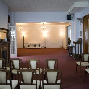 Empty church hall with rows of chairs facing a lit stage and burgundy carpet