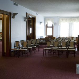 Empty meeting room with rows of chairs on a maroon carpet and bright windows at the back