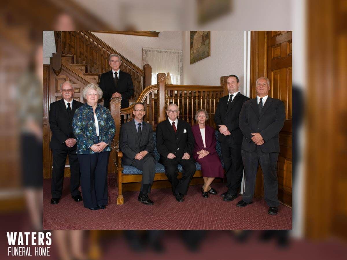 Group of eight people posing on a staircase and carpeted hallway in a historic building, with a “WATERS” logo
