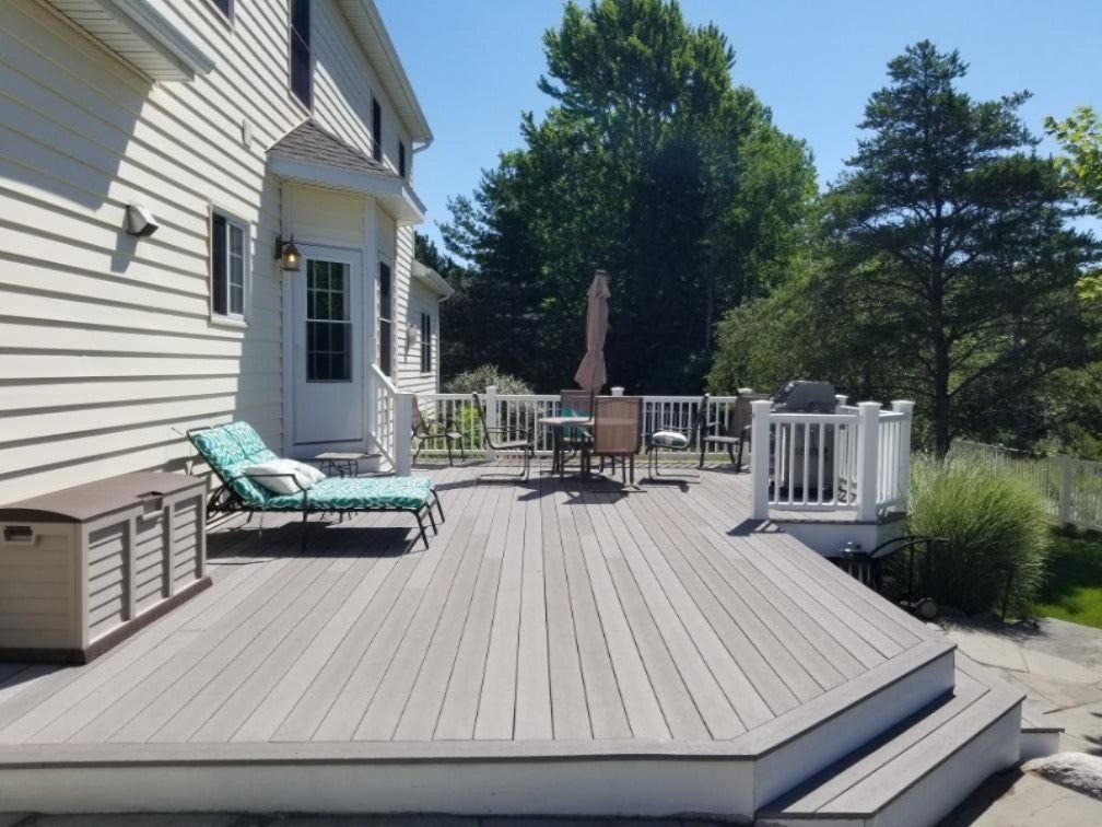 Wooden deck with lounge chairs beside a white house, overlooking trees and a fenced yard