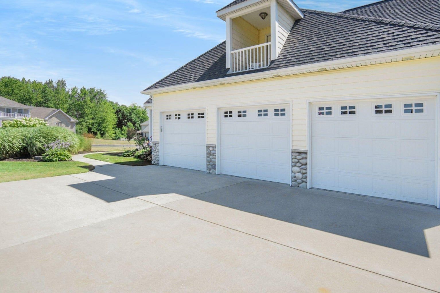 A white house with three garage doors and a balcony.