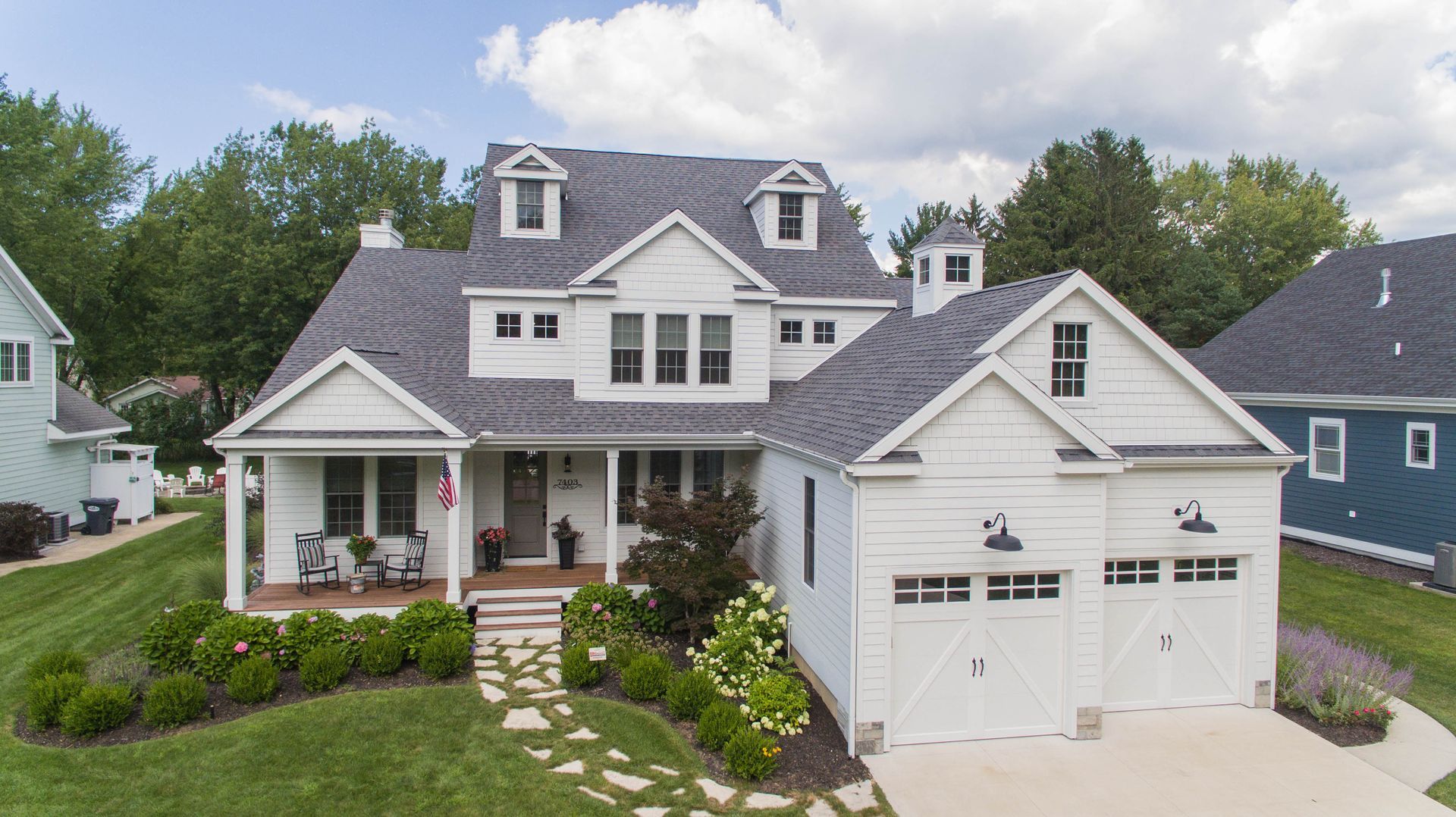 Gray two-story house with white trim, front porch, and double garage in a landscaped suburban setting
