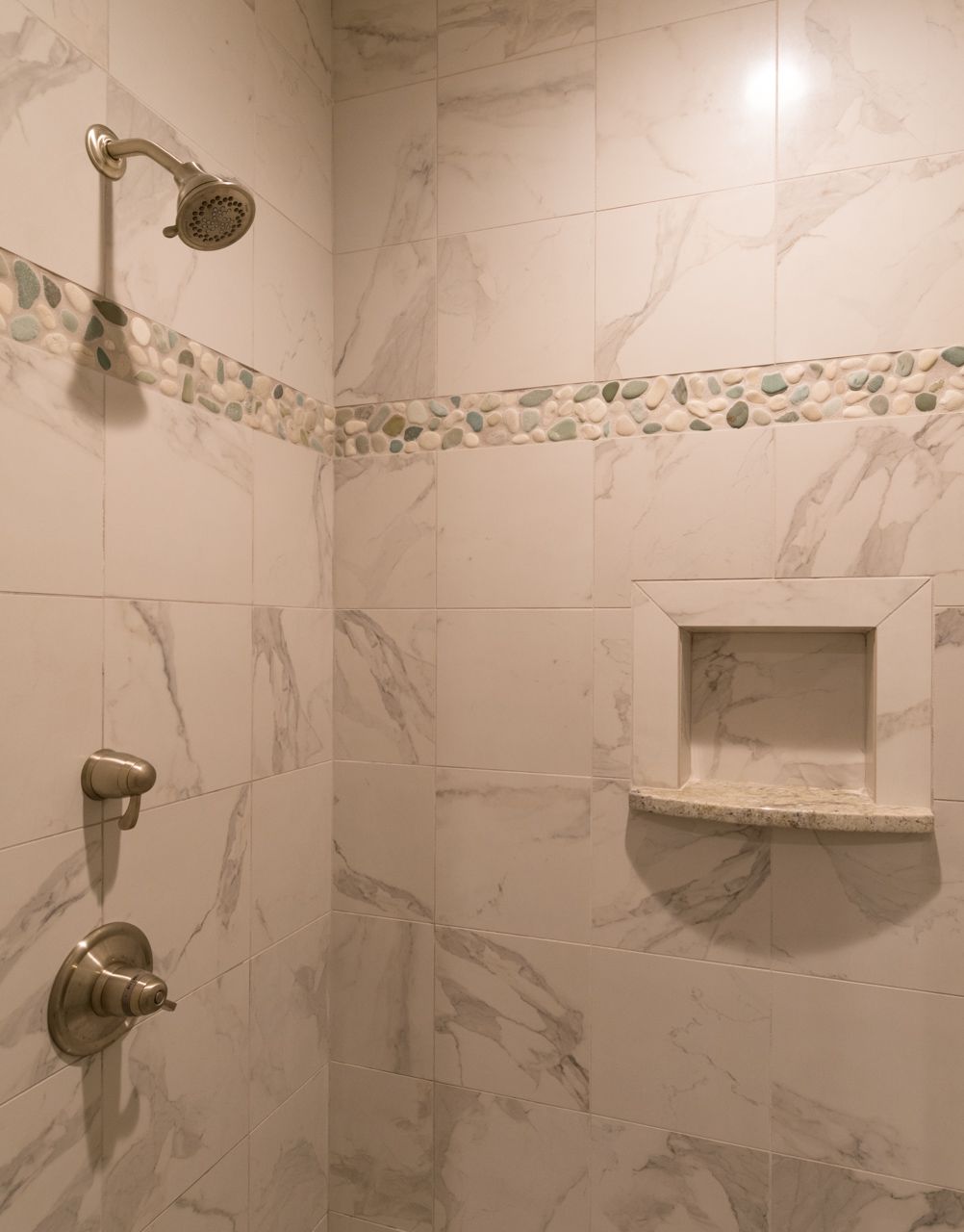 A shower with a shower head and a shelf in it.