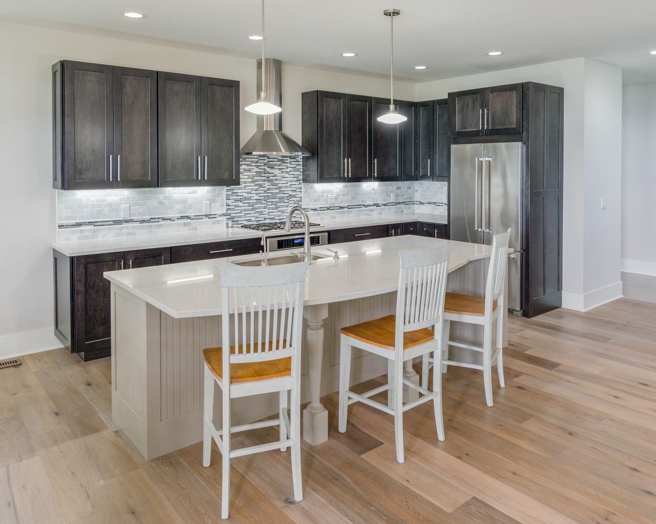 A kitchen with a large island , stools and a refrigerator.