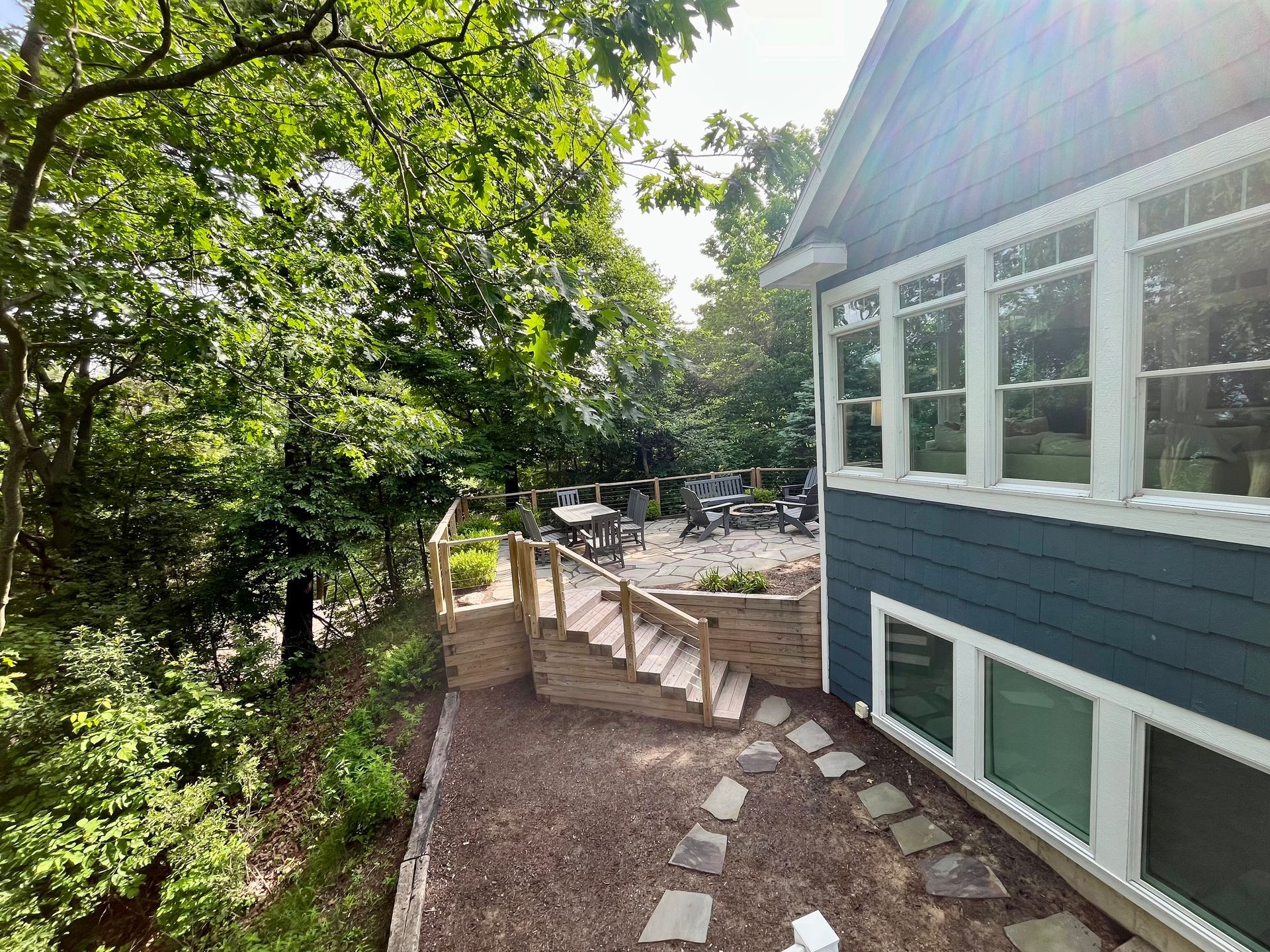 A blue house with a patio and stairs in front of it surrounded by trees.