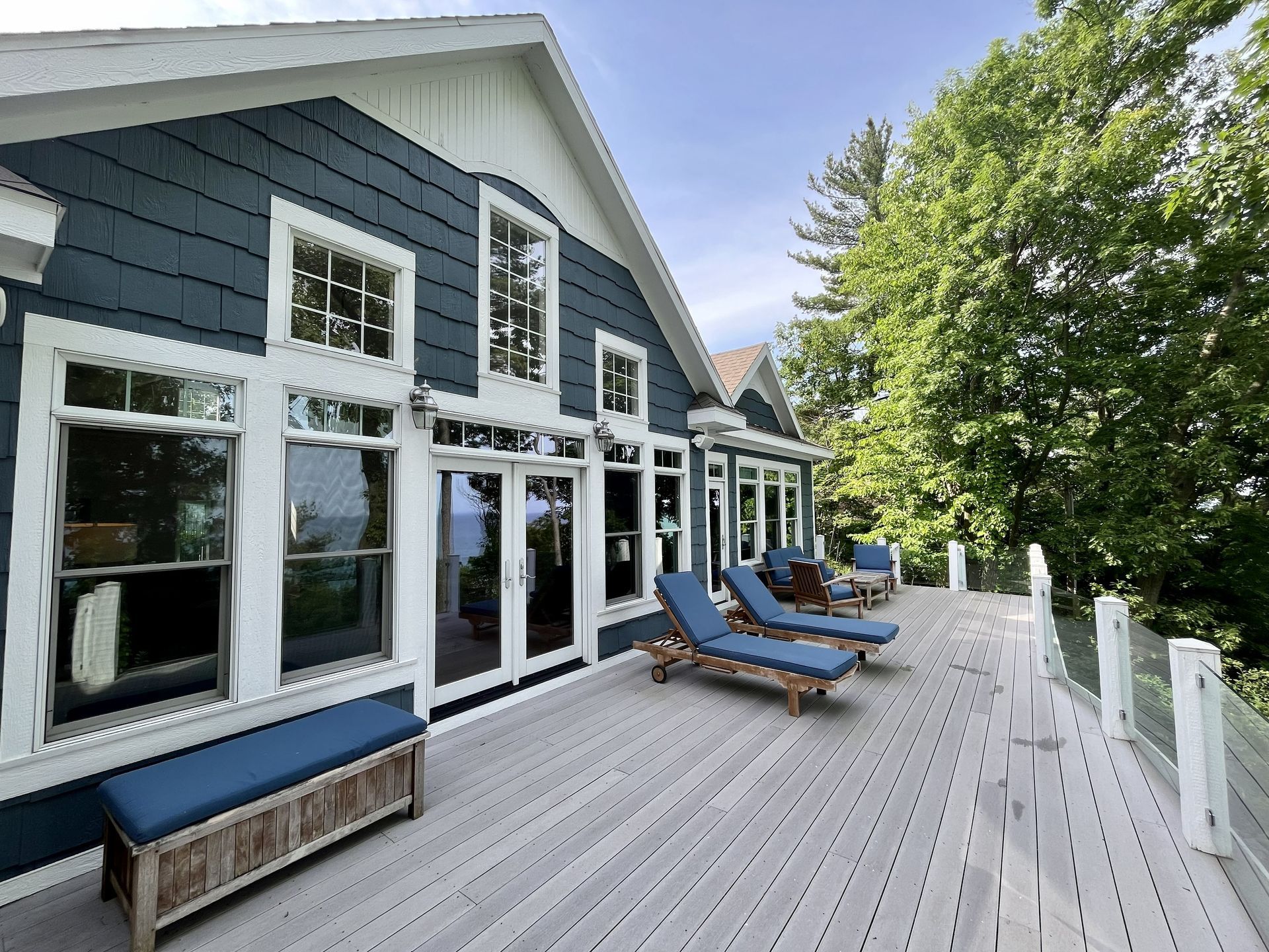 Blue house deck with lounge chairs and white railings beside green trees