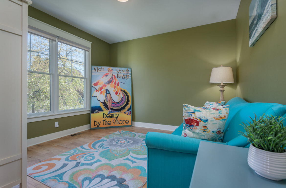 A living room with green walls , a blue couch , a rug , a lamp , and a painting.
