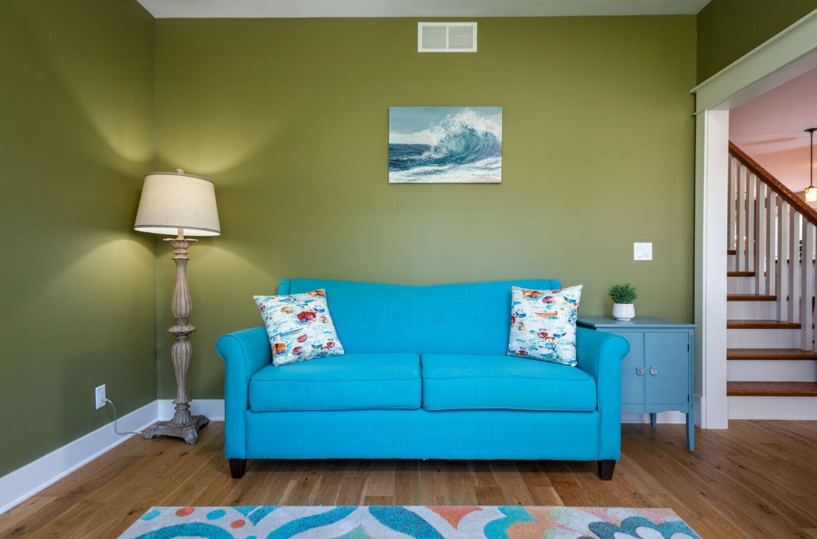 A living room with a blue couch , lamp , and stairs.
