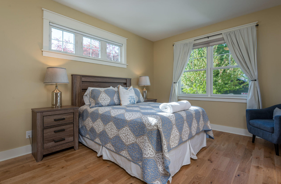 A bedroom with a bed , nightstand , chair and window.