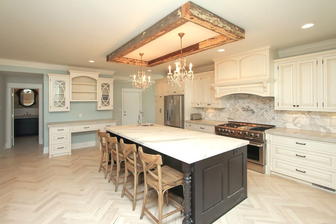 A kitchen with white cabinets , a large island , a stove , and a chandelier.
