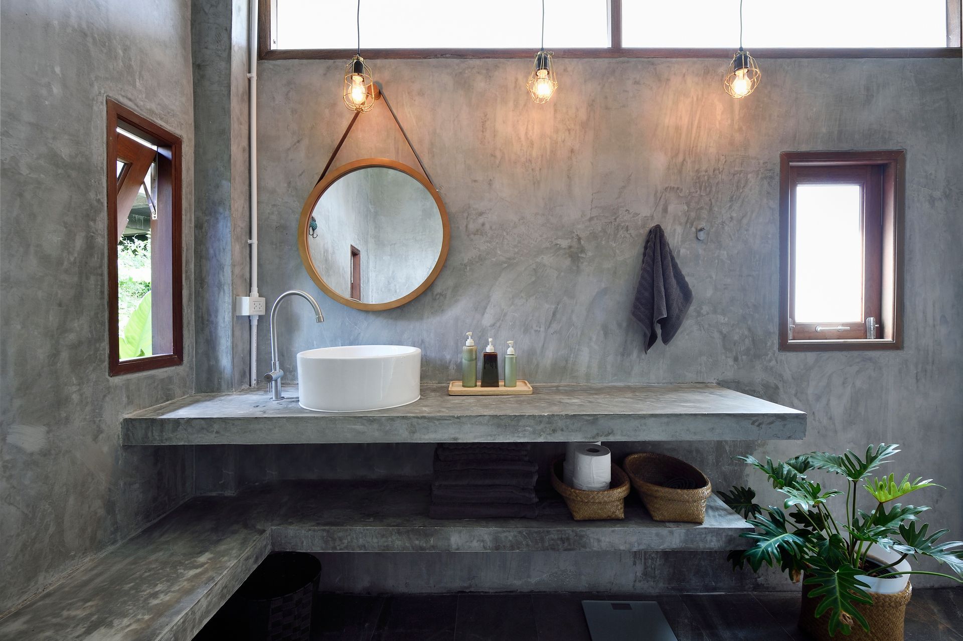 Modern bathroom with concrete walls, a round mirror, and a white sink.