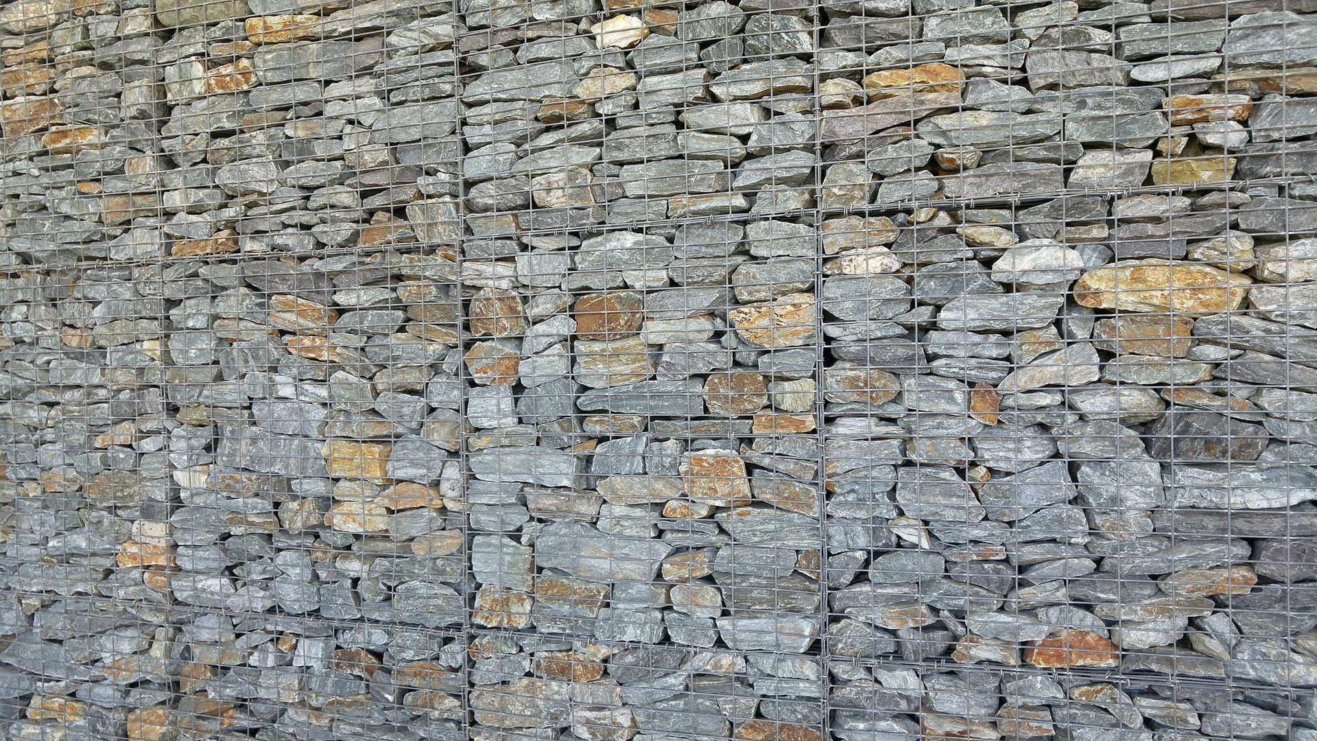 Grey and tan stone wall held in place by wire mesh.
