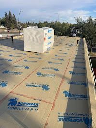 A flat roof with insulation installed; a stack of more insulation sits atop it, sunny day.