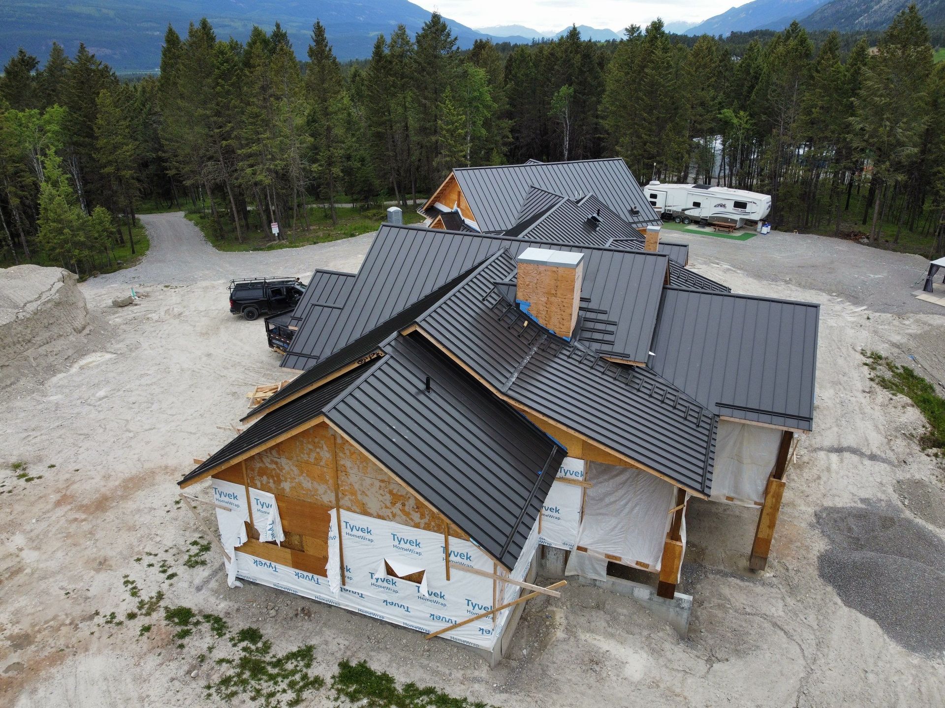 A house under construction with a dark roof, surrounded by dirt and trees.