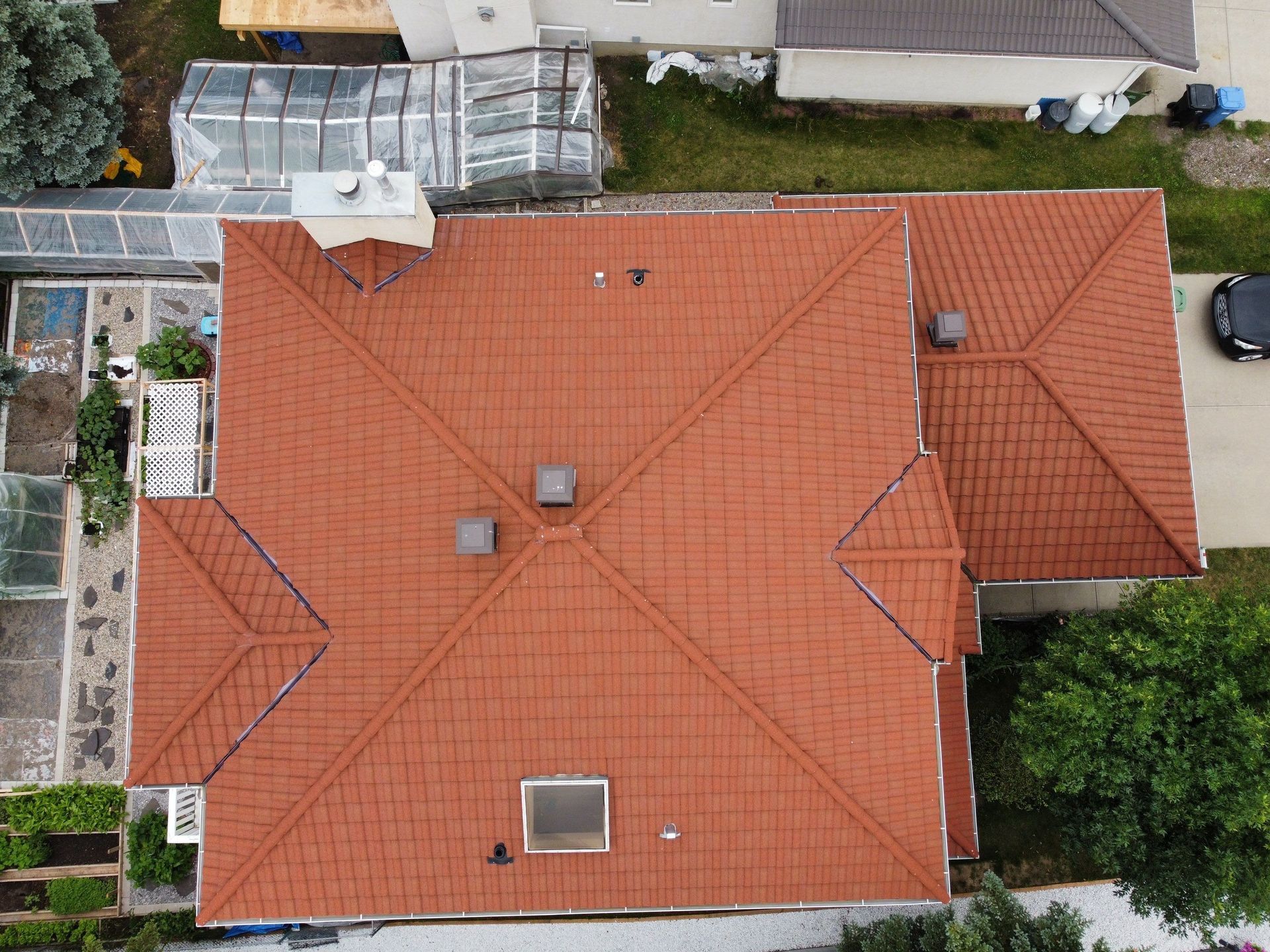 Overhead view of a red-roofed house with chimneys, a small window, and surrounding greenery.
