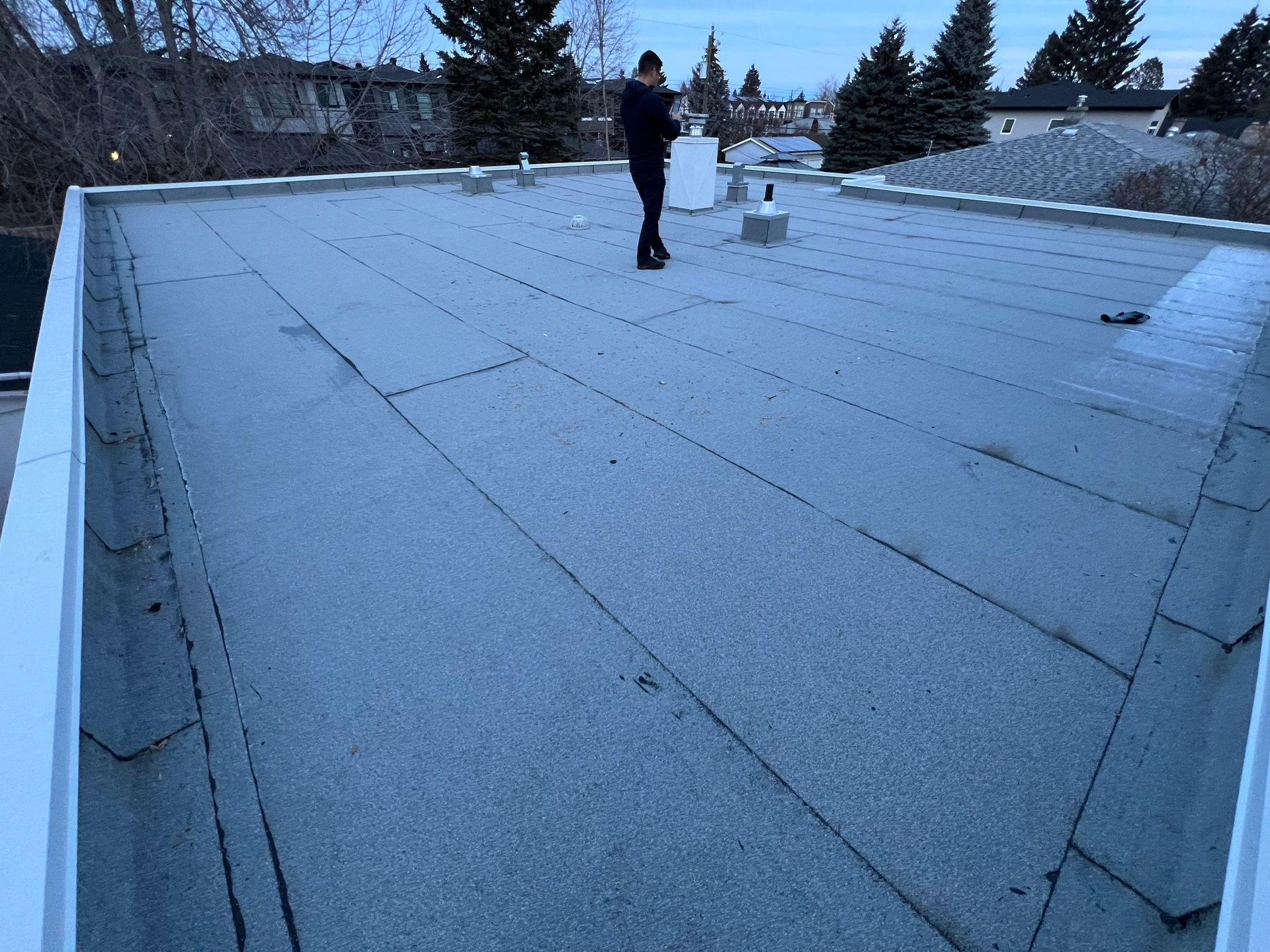 Person standing on a gray flat roof in a residential area with a cloudy sky in the background.